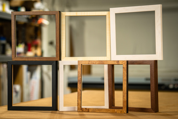 Modern picture frames stacked upright in walnut, natural maple, white, black and burl wood finishes